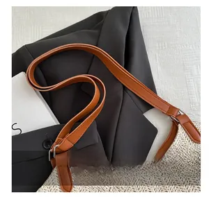 Detail of woven straw tote bag with brown leather adjustable strap and metal buckle