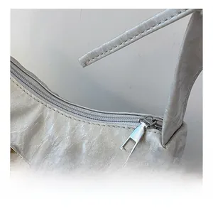 Detail of silver pleated shoulder bag featuring smooth metal zipper and butterfly charm
