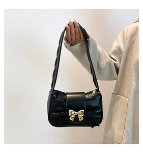 Detail of black leather underarm bag featuring a gold bow buckle and wide shoulder strap