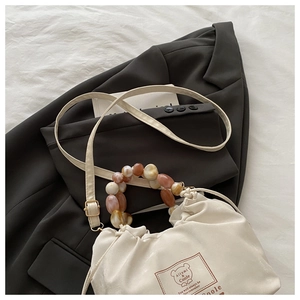 Detail of beaded handle on cream silk handbag with adjustable crossbody strap