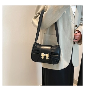 Detail of black pleated shoulder bag with golden bow metallic buckle and wide strap