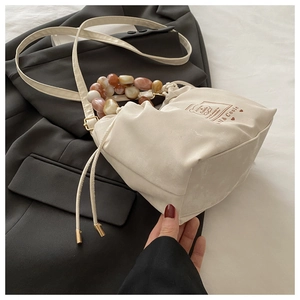 Detailed close-up of cream beaded handbag featuring large stone-pattern beads and drawstring
