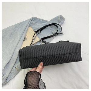 Detail of black textured tote bag with metal chain strap on a white fabric background