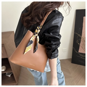 Detailed view of brown leather tote bag handle featuring a decorative floral silk scarf