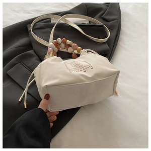 Detail of cream drawstring handbag featuring marble bead handle and printed brand logo