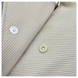 Macro detail of high-density canvas texture and silver magnetic snap closure on bag