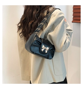 Detail of a black pleated baguette bag featuring a decorative golden metal bow knot