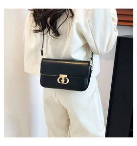 Detail of minimalist black shoulder bag with gold T-shaped clasp on female model