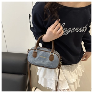 Détail du sac Boston en denim bleu avec anses en cuir marron et lettrage doré chic