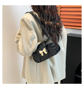 Detailed view of black underarm bag with gold bow buckle and pleated texture on model
