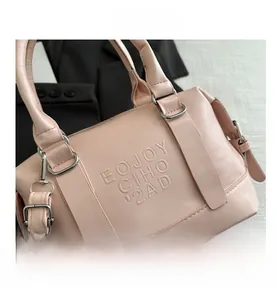 Détail du sac Boston en cuir rose avec logo embossé et boucles métalliques argentées