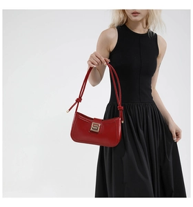 Detailed view of a red leather underarm bag with gold S-shaped buckle on a black dress