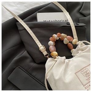 Detail of cream drawstring tote bag with marble texture beaded handle and brand print