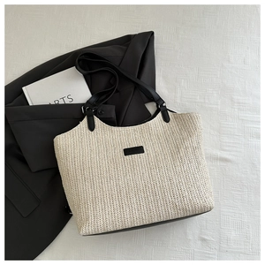 Detail of woven straw tote bag with black leather handles and contrast trim details