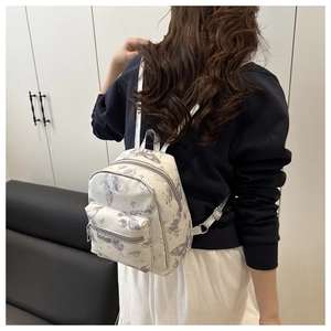 Detailed view of white mini backpack with butterfly print worn on shoulders by a model