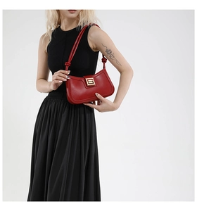 Close-up of red crescent shoulder bag with elegant gold buckle on a model shoulder