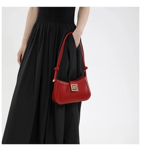 Detail of red glossy shoulder bag with gold metal buckle and knotted strap accents