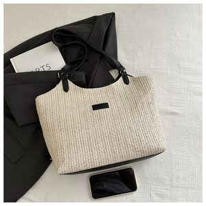Close-up of woven straw tote bag featuring black PU leather trim and chic handle details