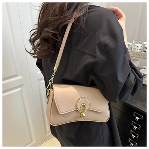 Beige faux leather shoulder bag with gold circular buckle worn by model in a cafe setting