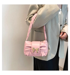 Detailed shot of pink pleated baguette bag with gold bow ornament and leather handle