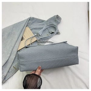 Detail of light blue textured messenger bag with silver metal chain strap and woven fabric
