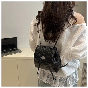 Detail of heart-quilted black mini backpack featuring metal chain straps and turn-lock