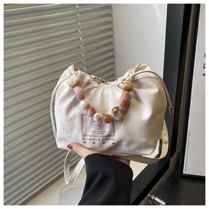 Detail of cream drawstring bucket bag featuring amber and pink beaded handle strap