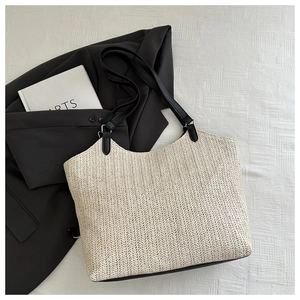 Detail of hand-woven straw tote bag featuring contrast black leather handles and silver buckles
