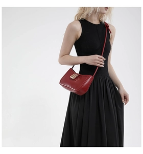 Macro view of red matte leather bag featuring a gold buckle and knotted shoulder strap