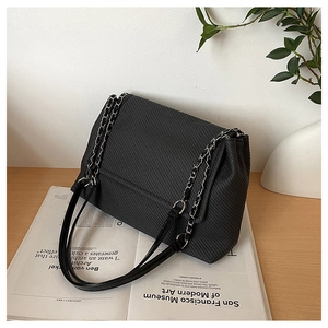 Detail of black flap shoulder bag with textured weave and silver metal chain strap
