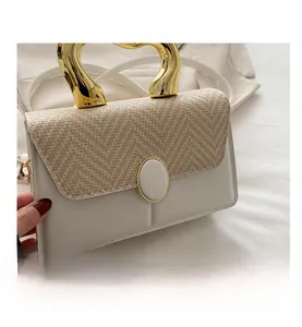 Detail of woven and white leather crossbody bag featuring a unique gold heart handle