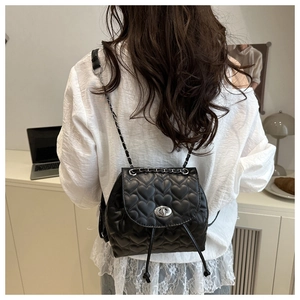 Detail of black heart-quilted mini backpack with silver twist lock on female model