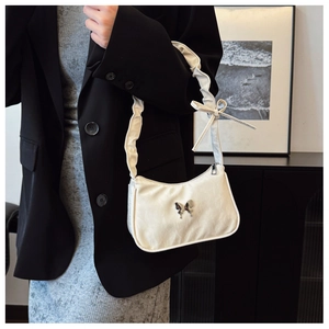Detail of white pleated shoulder bag featuring a silver butterfly charm and knotted strap