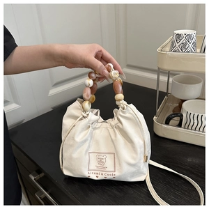 Detail of beaded handle and drawstring bucket bag with branded label on soft fabric