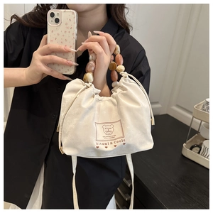 Detail of cream drawstring pleated bag featuring amber acrylic beaded handle and soft suede texture