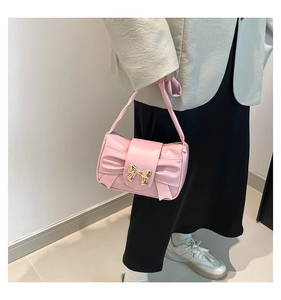 Pink shoulder bag with golden bow buckle and pleated accents shown on model shoulder