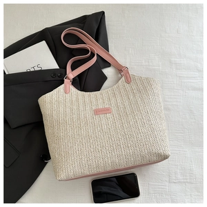 Close-up of woven straw tote bag featuring pink leather trim and fashion patch detail