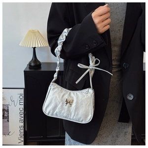 Detail of silver metallic shoulder bag featuring a butterfly buckle and ruffled strap