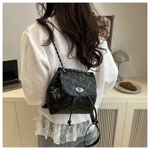 Detail of a mini black heart-quilted backpack with silver chain straps and a twist-lock