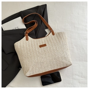 Close-up of woven straw tote bag featuring brown leather trim and FASHION embossed label