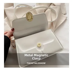 Detail of the golden magnetic buckle on a white leather shoulder bag with flap closure