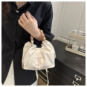 Detail of cream drawstring bag featuring marble-beaded handle and bear label patch
