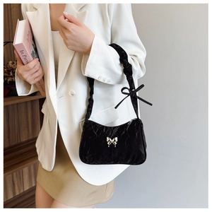 Close-up of black pleated velvet shoulder bag with metal butterfly detail and bow strap