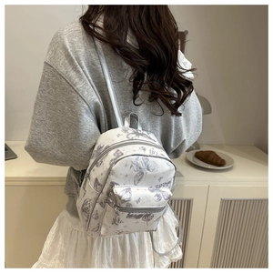 Miniature white backpack with grey butterfly print shown on a model in a cozy setting