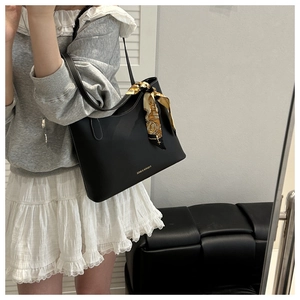 Detail of a black leather tote bag with white stitching and floral scarf on a model