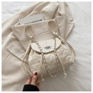 Detail of cream heart-quilted backpack with metal twist lock and silver chain strap