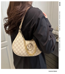 Detail view of cream monogram underarm bag featuring a chunky gold chain and M logo