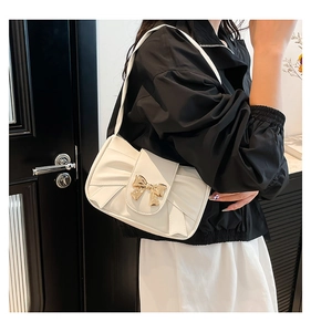 Detail of white pleated handbag featuring a golden bow metal clasp and PU leather texture
