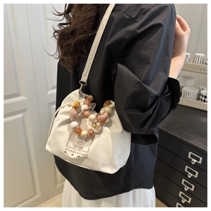 Detail of a creamy white drawstring dumpling bag featuring a retro beaded top handle