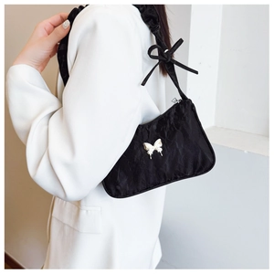 Detail of black pleated shoulder bag featuring a silver metal butterfly and bow accent